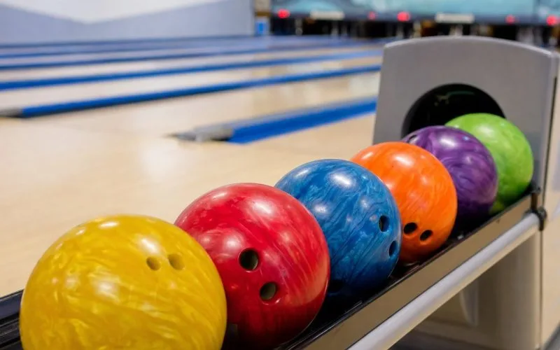 Bowlingbälle in verschiedenen Farben auf der Ballrückführung einer Bowlingbahn