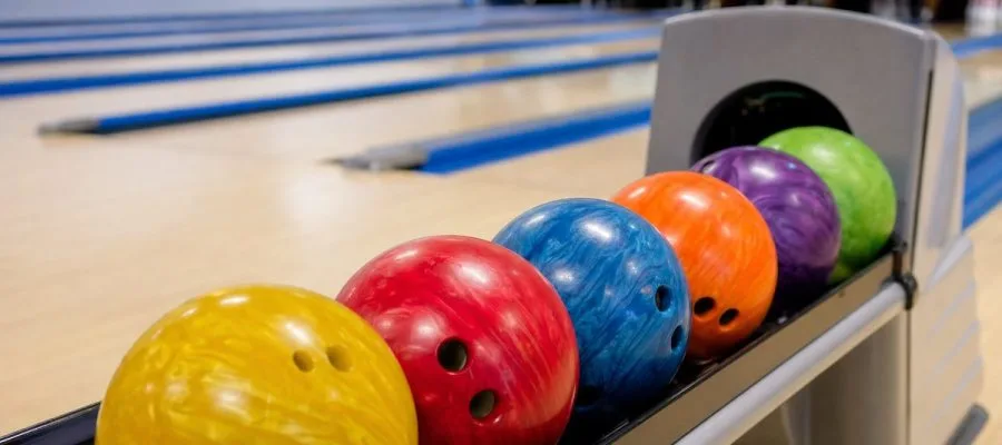 Bowlingbälle in verschiedenen Farben auf der Ballrückführung einer Bowlingbahn